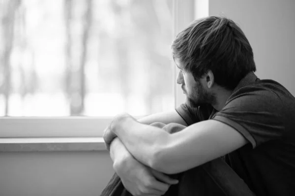 Trauriger junger Mann sitzt auf dem Boden und schaut durch das Fenster — Stockfoto