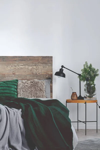 Yerba matt, gran i glasvas och svart industrilampa på nattduksbord i trä bredvid sängen — Stockfoto