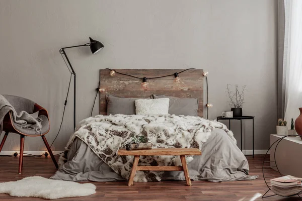 Teplý interiér ložnice s king size postelí s dřevěnou čelem se světlem, zuřivou přikrývkou a černým nočním stolkem — Stock fotografie