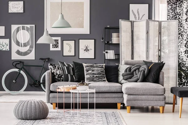 Meja kopi bergaya dengan vas dan piring di sebelah sofa sudut Skandinavia abu-abu dengan bantal di interior monokromatik — Stok Foto