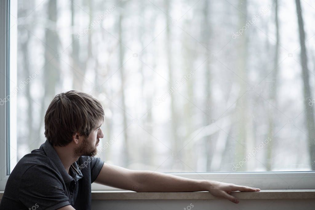 Young man sitting on the floor of living room with big window