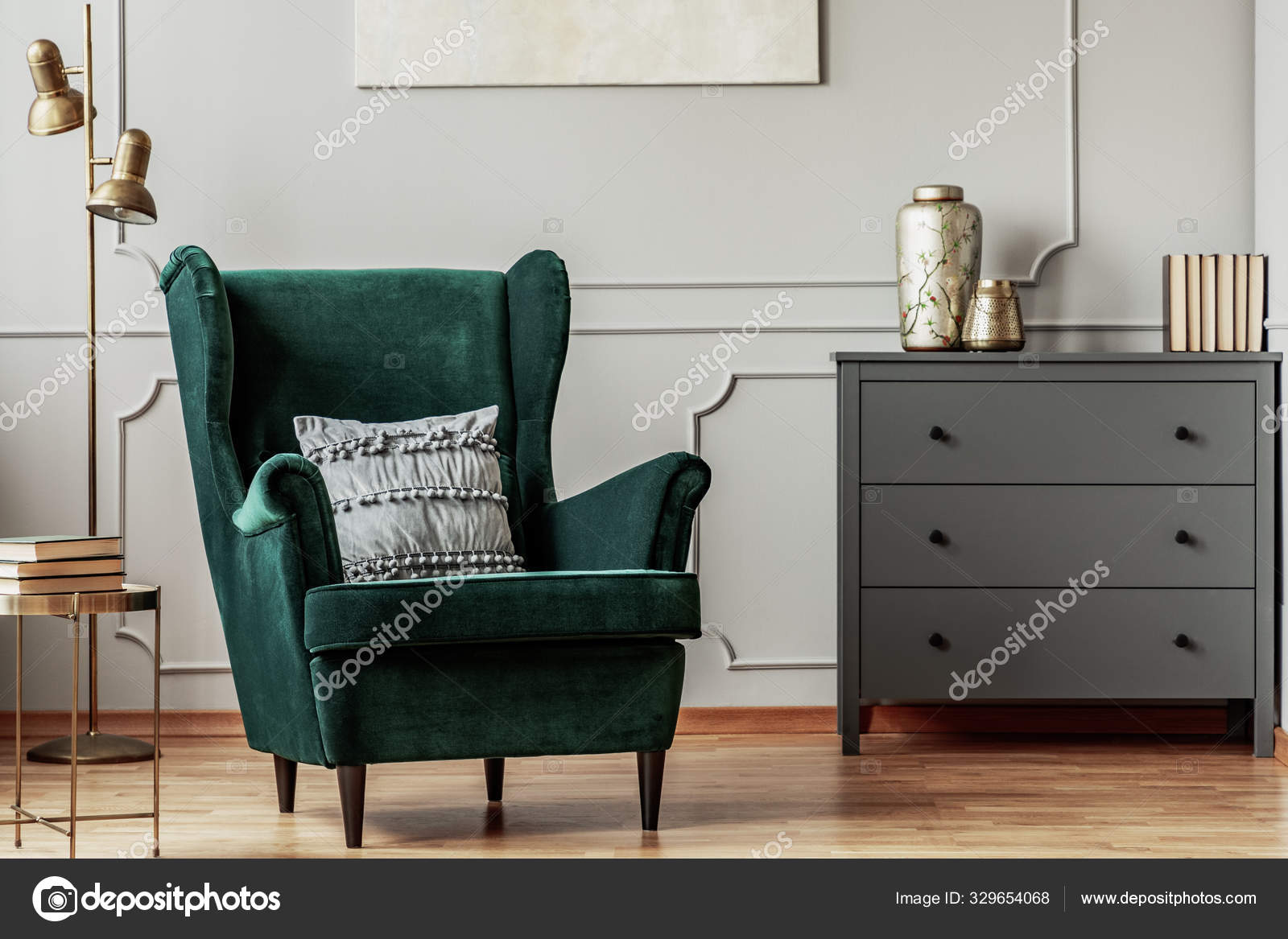 emerald green wing back chair with pillow in grey living room interior with  wooden commode 329654068
