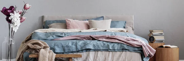 Flores em vaso de vidro ao lado da cama king size com cama pastel rosa, azul e bege no interior do quarto elegante — Fotografia de Stock