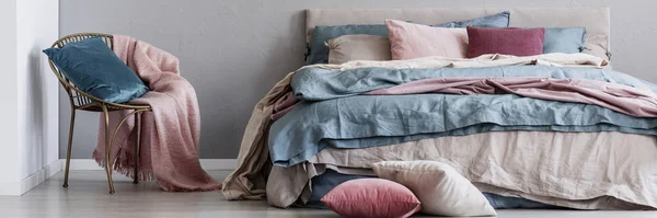 Trendy golden chair with pastel pink blanket and blue pillow next to big comfortable bed — 스톡 사진