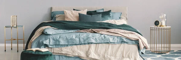 Кровать King size с бежевыми, синими и изумрудно-зелеными подстилками между двумя стильными тумбочками в модной спальне — стоковое фото