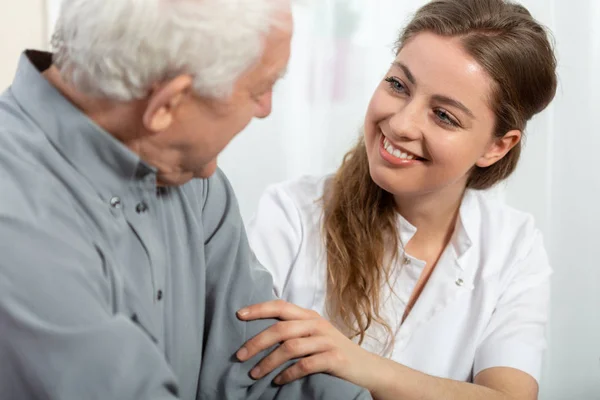 Lachende jonge verpleegster zittend aan tafel met senior patiënt — Stockfoto