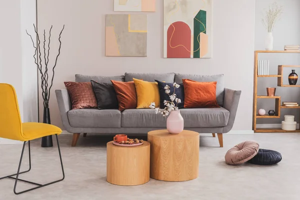 Foto real de mesas redondas de madera frente a un sofá gris con almohadas de colores en el interior luminoso de la sala de estar —  Fotos de Stock