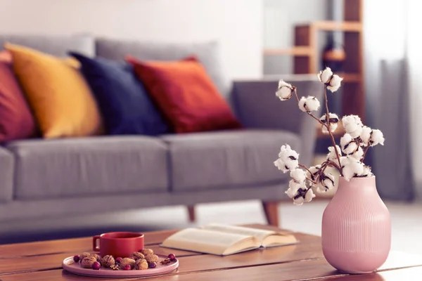 Close-up de flores de algodão em um vaso rosa em pé sobre uma mesa de café de madeira com um elegante interior sala de estar no fundo — Fotografia de Stock