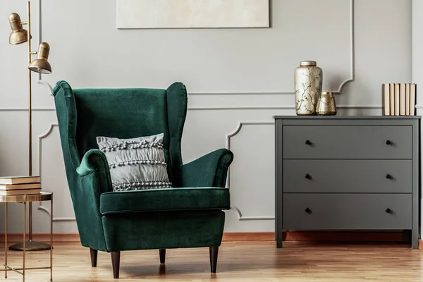 Silla trasera de ala verde esmeralda con almohada en el interior de la sala de estar gris con cómoda de madera —  Fotos de Stock