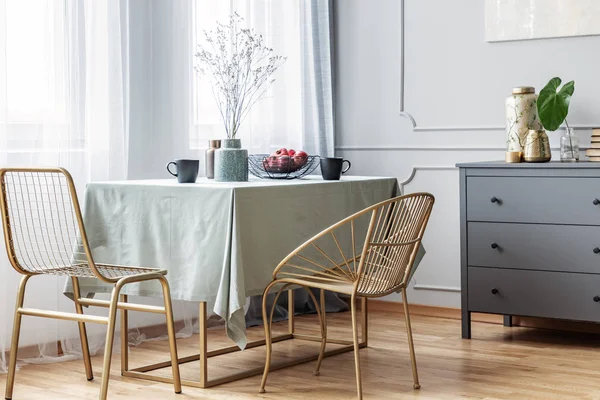 Long table, golden chairs and grey commode in beautiful living room interior