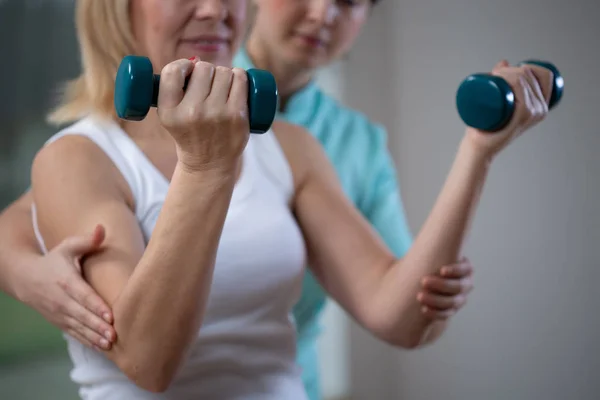 Physiothérapeute professionnel aidant la femme âgée à soulever des poids de la main — Photo