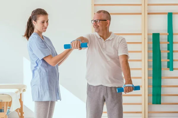 Physiotherapist assisting a senior patient performing weight exercises — 스톡 사진