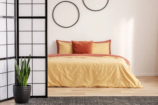 Черные обручи на белой стене в элегантной спальне с оранжевыми постельными принадлежностями на кровати — стоковое фото