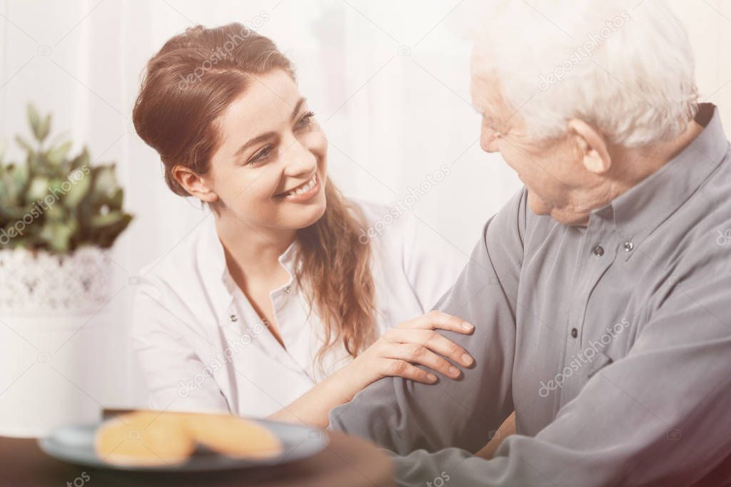 Beautiful volunteer smiling at senior man at nursing home