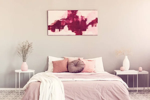 2つの白い工業用ナイトスタンドテーブルと花瓶の花の間にパステルピンクの寝具付きキングサイズベッド — ストック写真