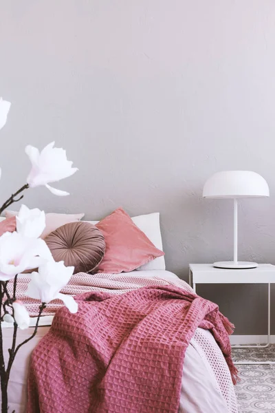 Biała lampa przemysłowa na prostym stoliku nocnym obok przytulnego łóżka z różową ściółką — Zdjęcie stockowe