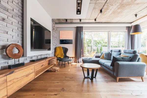Elegan ruang tamu dengan lantai kayu ringan, sofa abu-abu dan kursi belakang sayap dan TV besar di dinding — Stok Foto