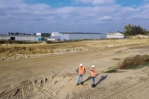 Vista superior de dos trabajadores de la construcción de carreteras en chalecos naranjas y cascos protectores en el centro en el campo —  Fotos de Stock