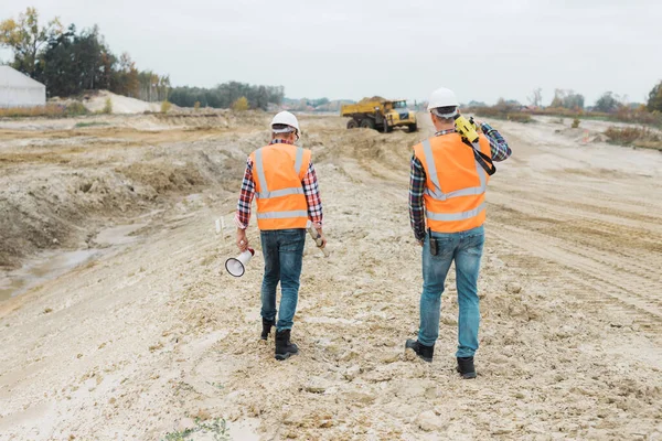 Two professional road construction workers in orange vests and protective helmets in the middle on the terrain — Stock Photo, Image