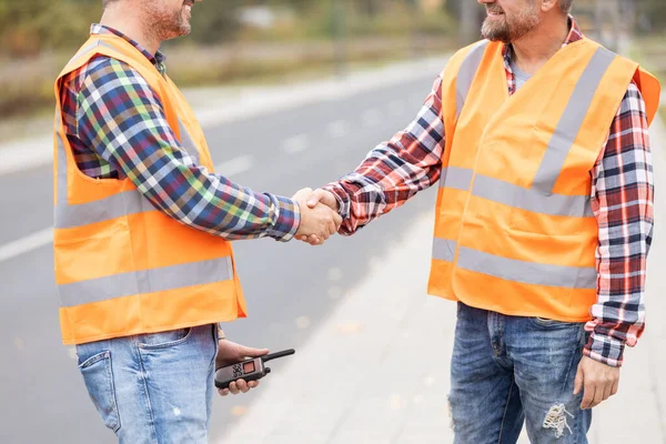 Due costruttori stringendo la mano sul campo della costruzione di strade — Foto Stock