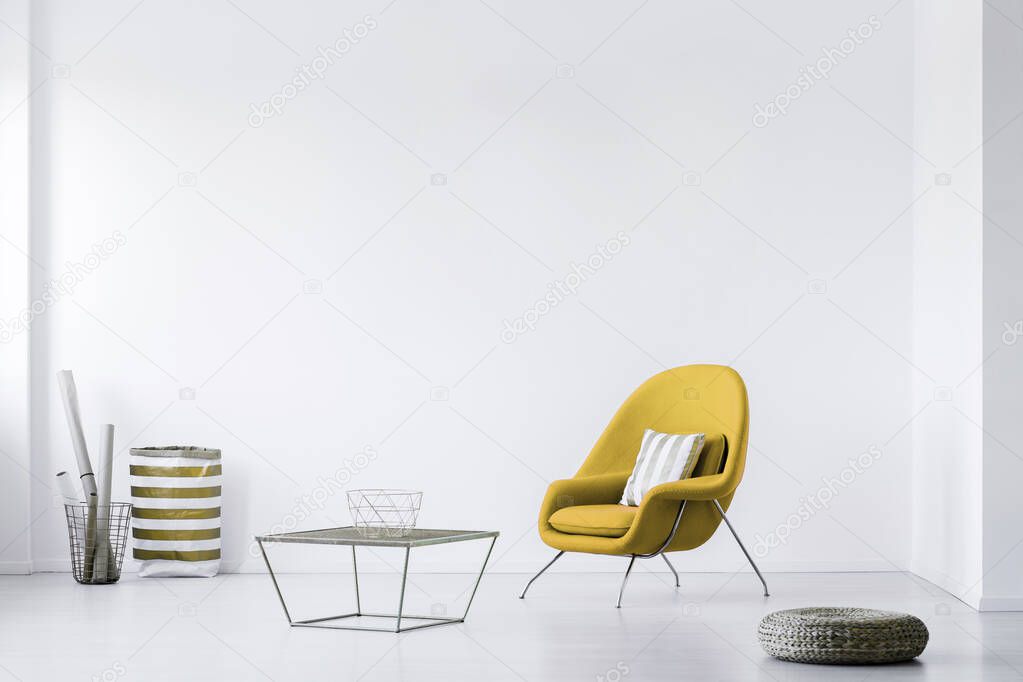 Real photo of a minimalistic living room interior with a yellow armchair. Empty, white wall. Place your poster