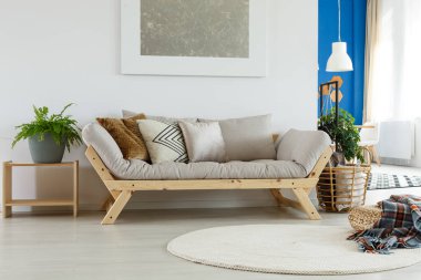 İçinde bej rengi İskandinav koltuğu olan şık bir oturma odası. Yastıkları var. Duvarında da gümüş soyut resim var.