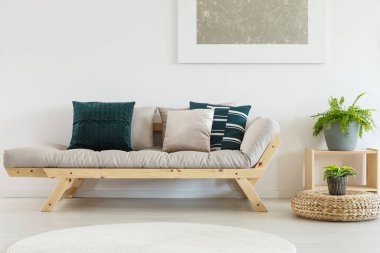 Bej koltuktaki yastıklar zevkli oturma odasının içinde ahşap tezgahta bitki var.