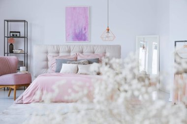 Şık yatak odasındaki kral yatağında pastel yatak örtüsü. Beyaz duvarda soyut pembe ve mor resim var.