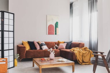 Sarı bir battaniyenin gerçek fotoğrafı. Kahverengi bir kanepede uzanmış. Parlak bir oturma odasında.