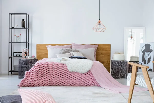 Satin beige pillows and fury white blanket on big warm bed in stylish bedroom interior, copy space on empty white wall