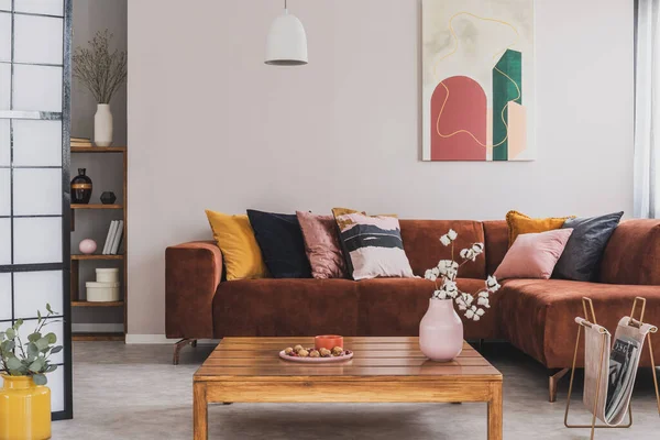 Foto real de una mesa cuadrada de madera frente a un sofá de gamuza marrón con cojines decorativos en el acogedor interior de la sala de estar —  Fotos de Stock