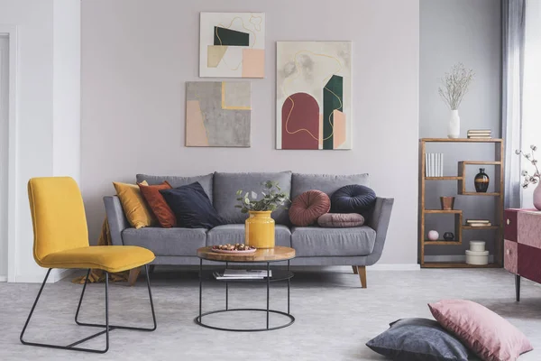 Foto real de una silla amarilla y un sofá gris con almohadas en un interior moderno de la sala de estar —  Fotos de Stock