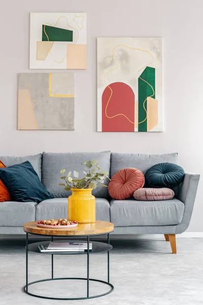 Foto real de una mesa de centro redonda con nueces y jarrón amarillo de pie frente a un sofá gris en el interior de una sala de estar —  Fotos de Stock