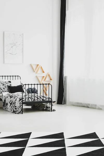 Mapa en marco blanco sobre cama de metal industrial con ropa de cama en blanco y negro y alfombra estampada en el suelo —  Fotos de Stock