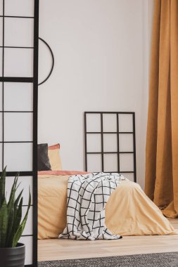 Yatağın yanındaki siyah ahşap ızgara. Yatak odasında beyaz duvarlı turuncu yatak.