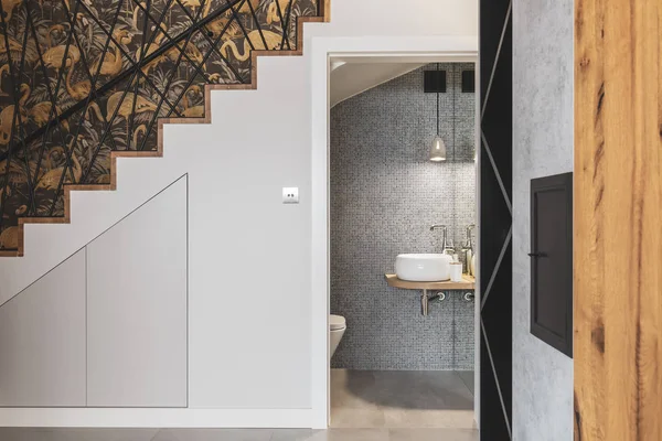 Couloir avec escalier et porte ouverte à une élégante salle de bain avec mur d'argent et lavabo blanc — Photo