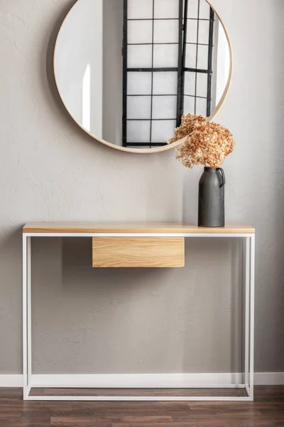 Elegante espejo redondo en marco de madera encima de la mesa de consola de lujo con flores en jarrón en el interior del dormitorio de moda con jarrón beige — Foto de Stock