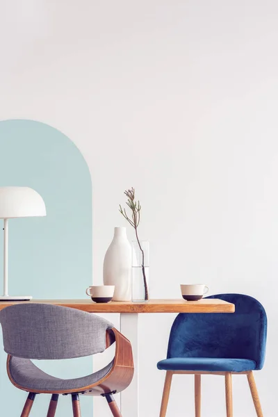 Stylish pastel pink and petrol blue chairs at long wooden table in bright dining room — ストック写真