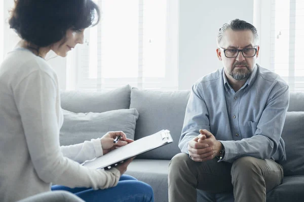 一个英俊的男人坐在灰色的沙发上与一位心理治疗师会面 — 图库照片