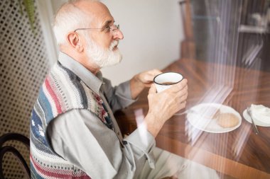 Yaşlı üzgün adam sabah kahvesini yalnız içiyor. 