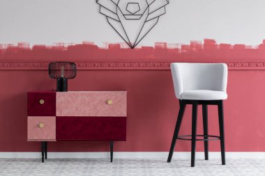 Pastel gri kadife sandalye. Pastel pembe ve bordo çekmeceli şık klozetin yanında.