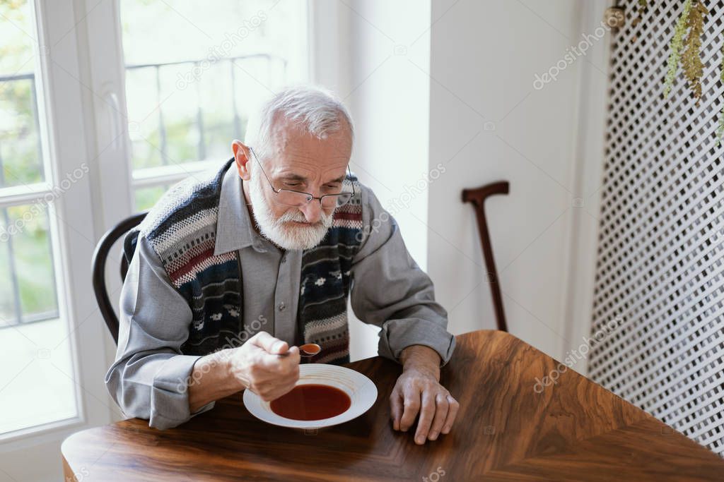Older sad man eating dinner by himself at home