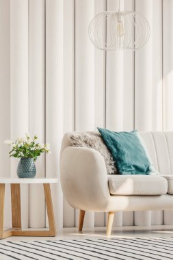 Parlak oturma odasının dikey görüntüsü, içinde çiçekli mavi vazo ve ahşap sehpanın yanında yastıklar olan şık bir kanepe.