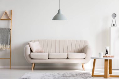 Beyaz kanepede, üzerinde kupalar olan ahşap sehpanın yanında, boş duvarda fotokopi odası olan gri lamba.