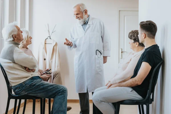 Starší Doktor Uniformě Mluví Svými Pacienty Čekajícími Chodbě — Stock fotografie