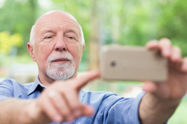 Gri adam sosyal medyaya koymak için cep telefonuyla selfie çekiyor.