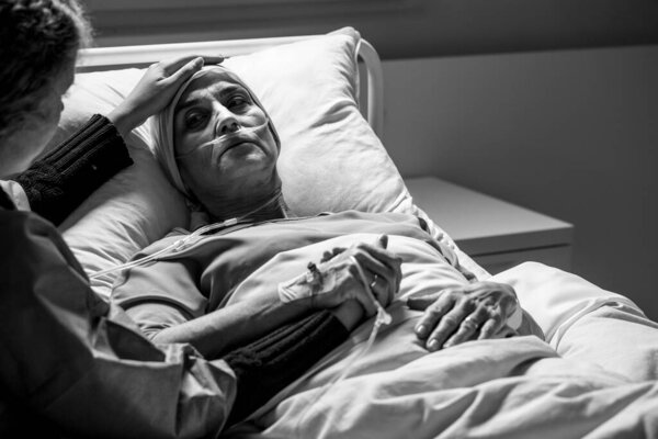 Daughter supporting sad, dying woman with tumor in a hospital, black and white photo