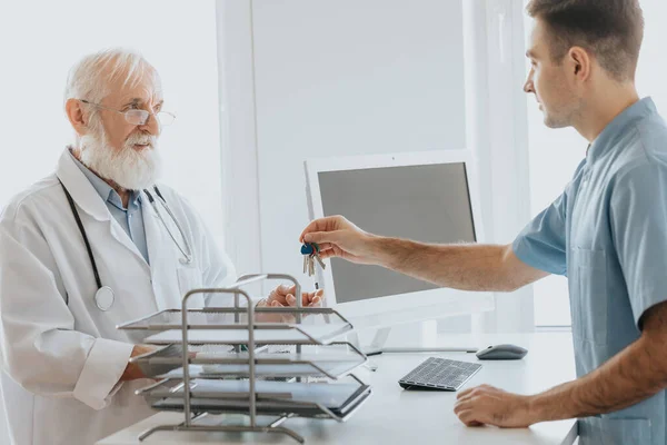 Junge Männliche Krankenschwester Gibt Älteren Arzt Die Schlüssel Zum Büro — Stockfoto