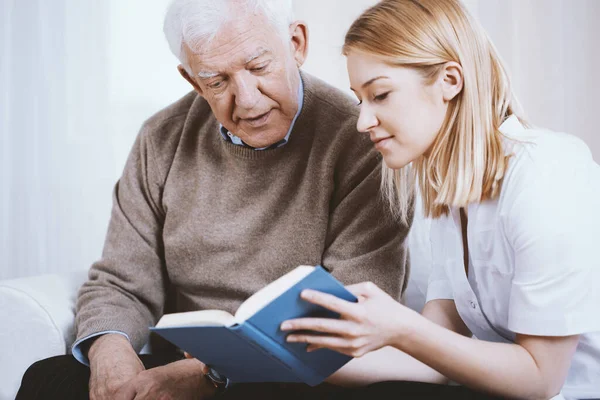 Young Blonde Volunteer Reading Book Senior Man Nursing Home — Stock Photo, Image