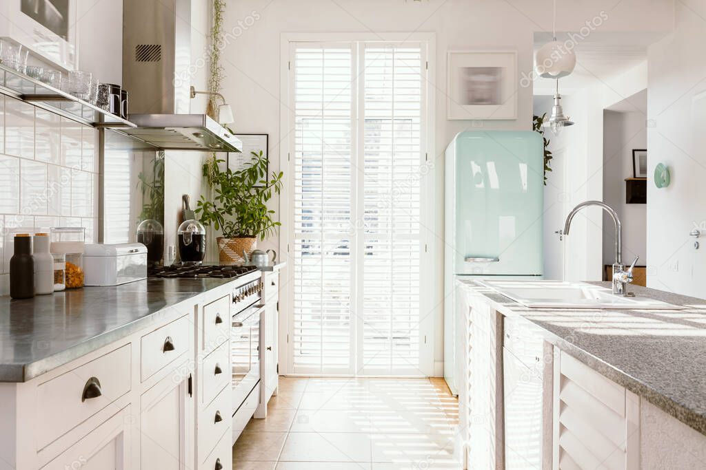 Bright kitchen interior with modern white furniture, pastel mint fridge and big floor to ceiling window